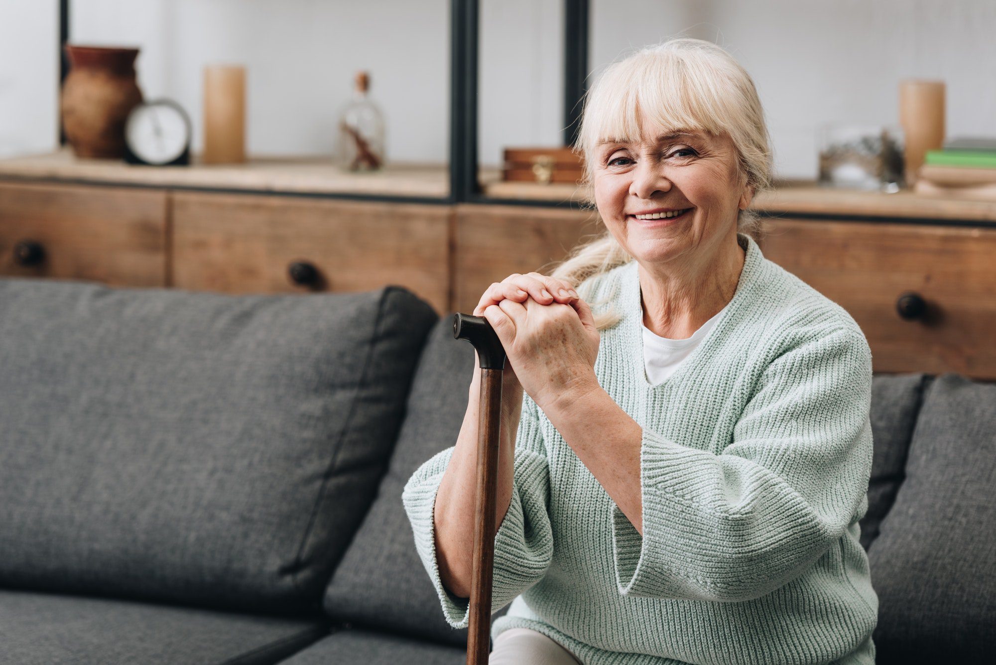 Cheerful senior woman sitting on sofa and holding walking stick on a Medicare Advantage Special Needs Plan.
