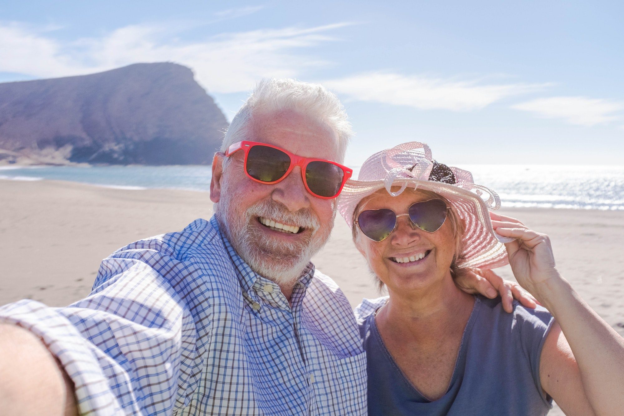 Couple of seniors traveling outside the U.S. and take a selfie on a beautiful beach with a mountain, knowing that their Medicare Supplement Plan has them covered.