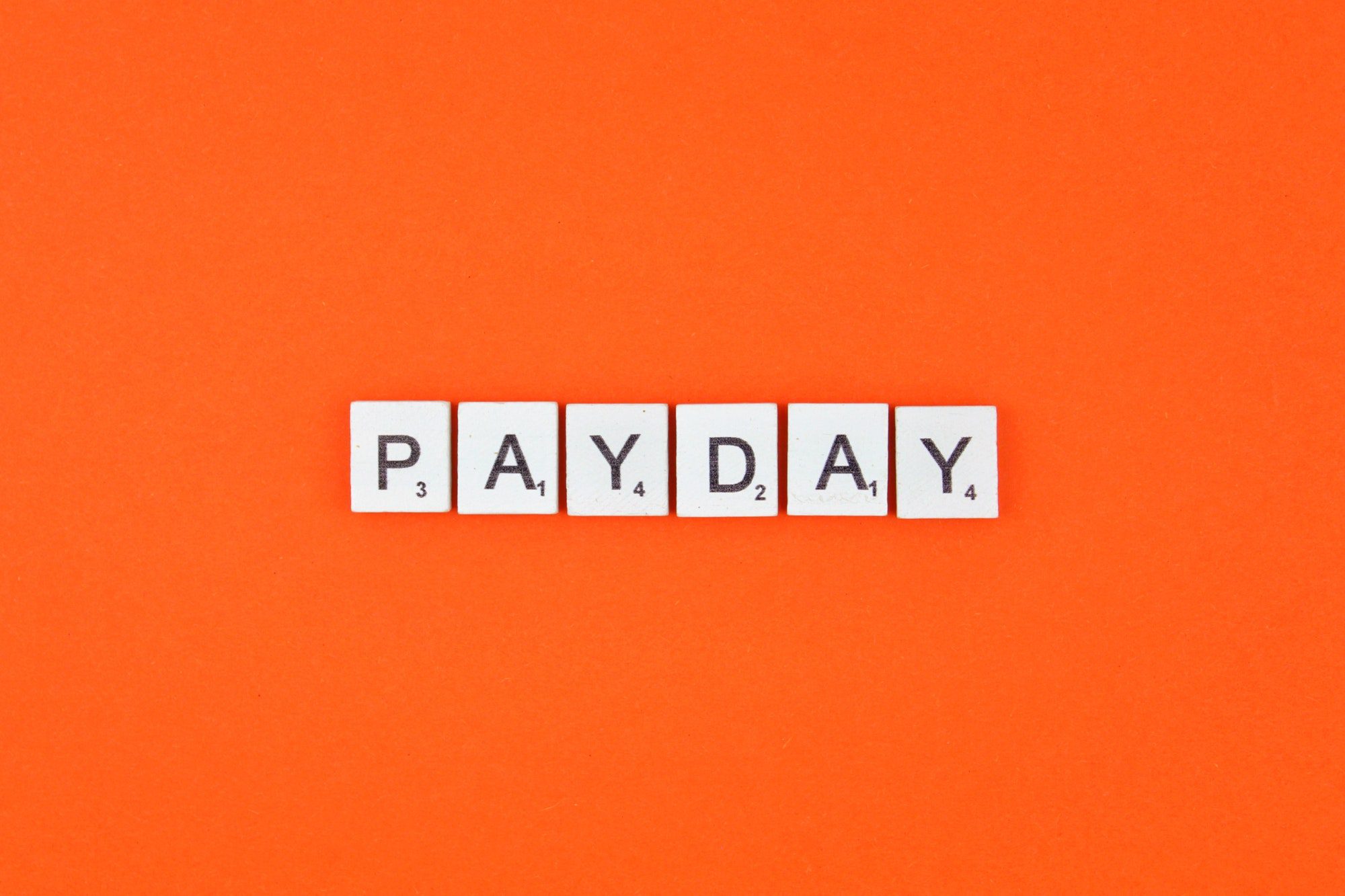 Payday scrabble letters word on an orange background referencing How are Insurance agents paid.