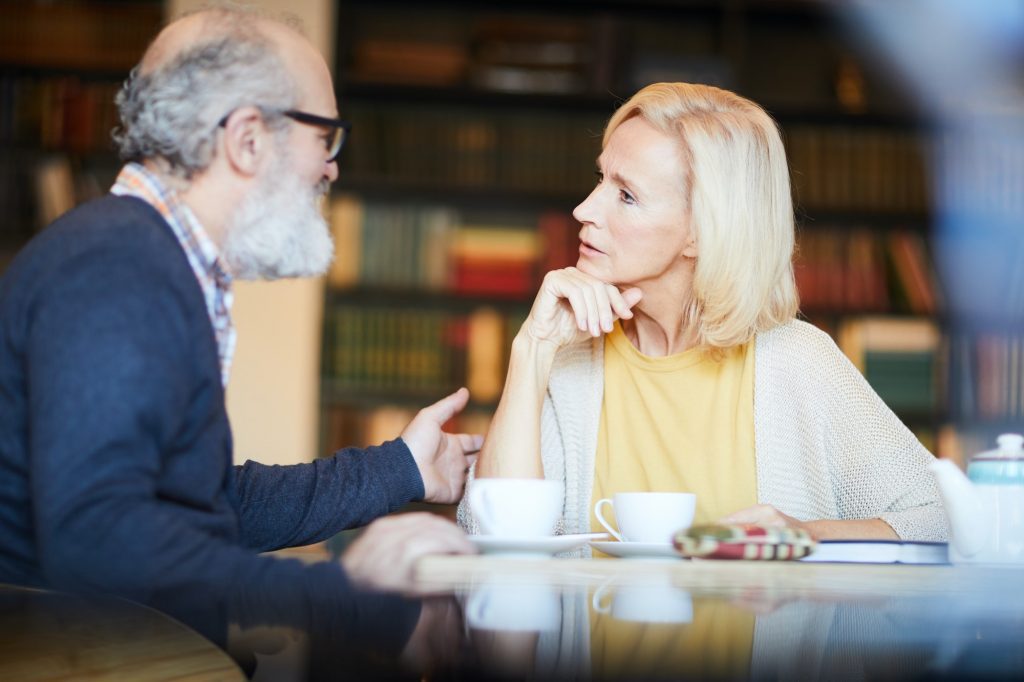 Senior man explaining underwriting to female friend as they share coffee.